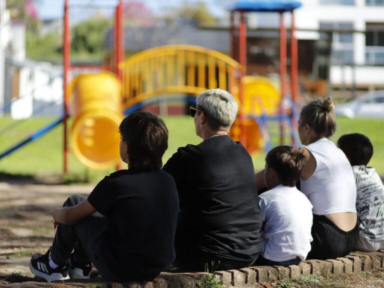 Niños y adolescentes junto a mujeres adultos, sentados en una plaza.